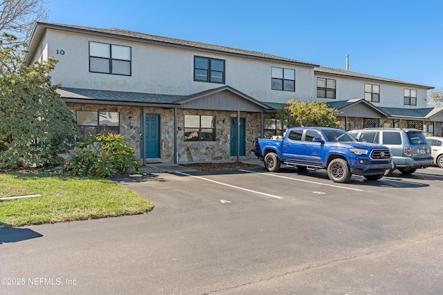 view of property with uncovered parking, stone siding, and stucco siding