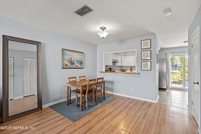 dining room featuring light wood-type flooring, visible vents, and baseboards