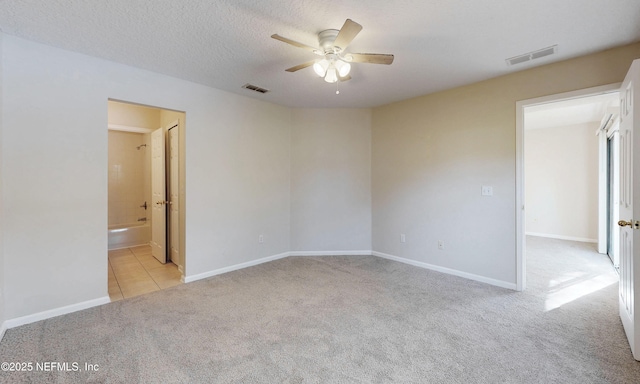 carpeted empty room with a textured ceiling, ceiling fan, tile patterned flooring, and visible vents