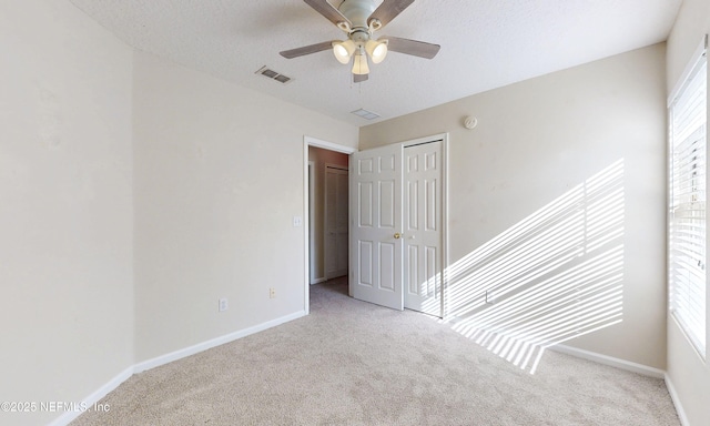 carpeted spare room featuring a textured ceiling, ceiling fan, visible vents, and baseboards