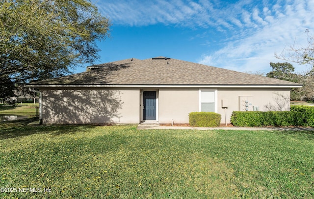 rear view of house with roof with shingles, a yard, and stucco siding