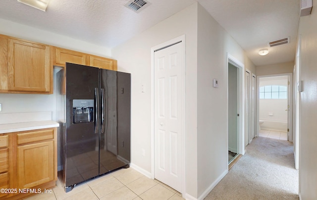 kitchen featuring light brown cabinetry, light countertops, black fridge with ice dispenser, and visible vents