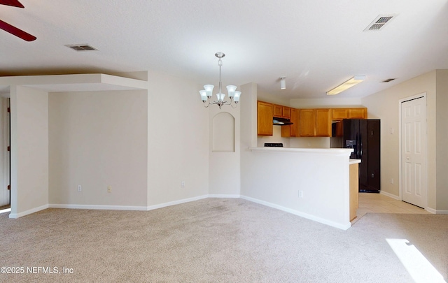 kitchen featuring visible vents, light colored carpet, a peninsula, black fridge, and ceiling fan with notable chandelier