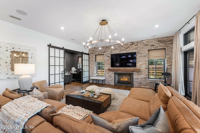 living room featuring a fireplace, a barn door, brick wall, wood finished floors, and a chandelier