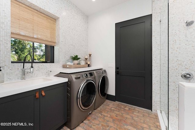 clothes washing area with brick floor, washer and dryer, laundry area, and a sink