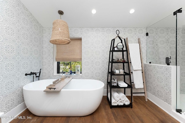 full bath featuring wood finished floors, a soaking tub, baseboards, and wallpapered walls