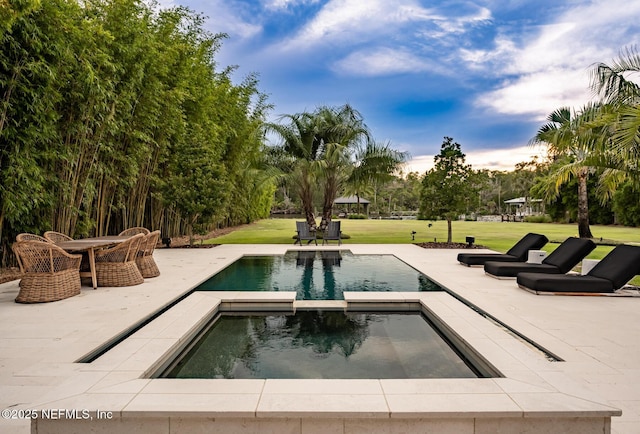 pool at dusk with outdoor dining space, a patio area, a lawn, and an in ground hot tub