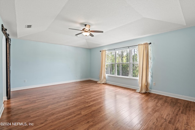 unfurnished room with a textured ceiling, a barn door, wood finished floors, visible vents, and a ceiling fan