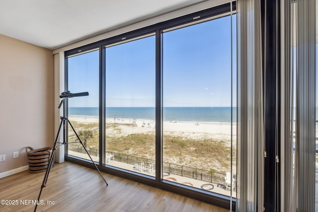 interior space with a wall of windows, a view of the beach, wood finished floors, baseboards, and a water view