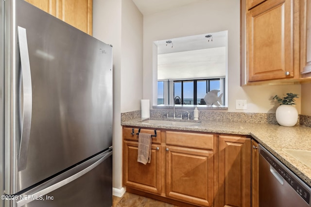 kitchen featuring brown cabinetry, appliances with stainless steel finishes, light stone countertops, and a sink