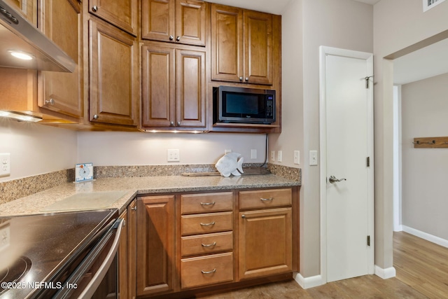 kitchen with baseboards, light wood finished floors, built in microwave, under cabinet range hood, and brown cabinets