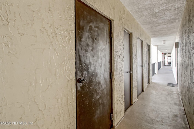 hallway with unfinished concrete flooring and a textured wall