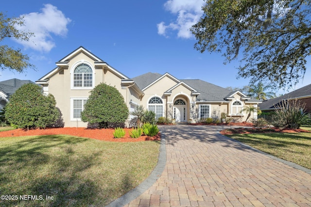 view of front of property featuring a front yard, decorative driveway, and stucco siding