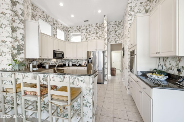 kitchen with wallpapered walls, light tile patterned floors, appliances with stainless steel finishes, a peninsula, and a sink