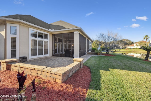 rear view of property featuring a lawn, a patio, a sunroom, roof with shingles, and stucco siding