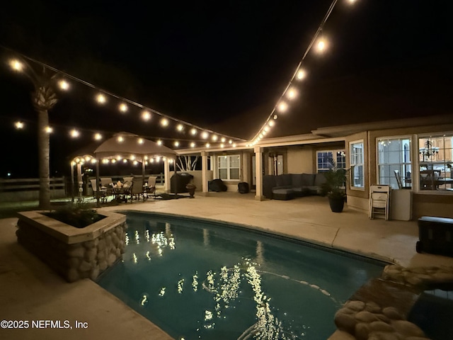 pool at night with outdoor lounge area, a patio area, and an outdoor pool