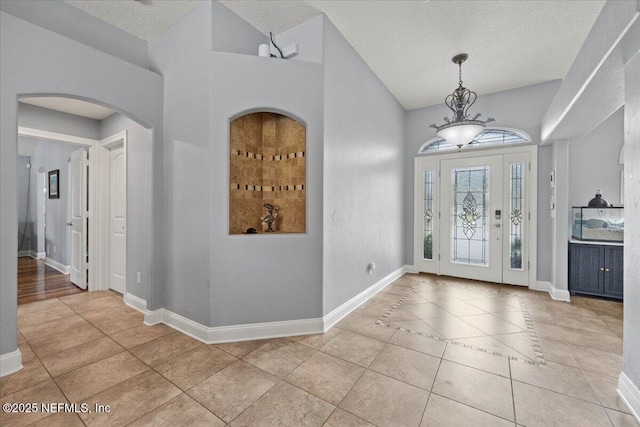 entrance foyer with light tile patterned floors, baseboards, arched walkways, and a textured ceiling