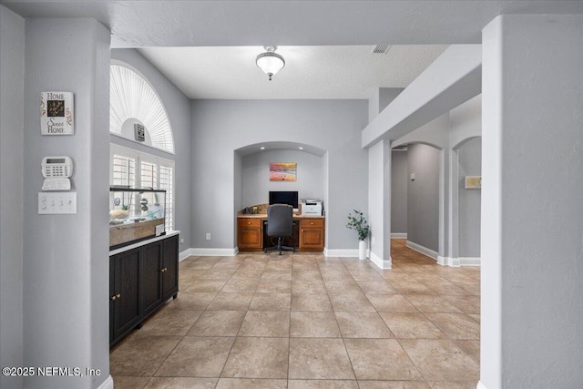 home office with arched walkways, visible vents, light tile patterned flooring, a textured ceiling, and baseboards