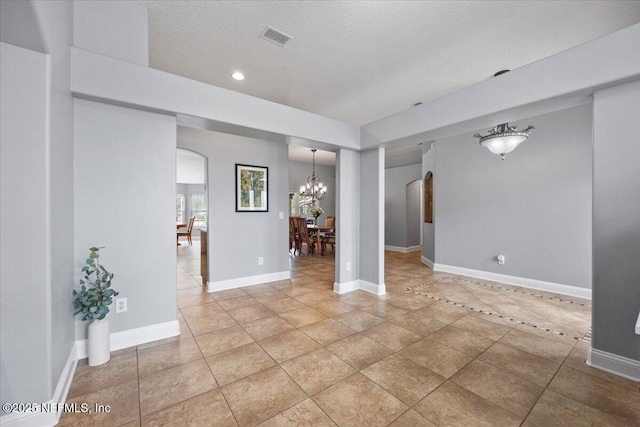 unfurnished room featuring arched walkways, a notable chandelier, visible vents, a textured ceiling, and baseboards