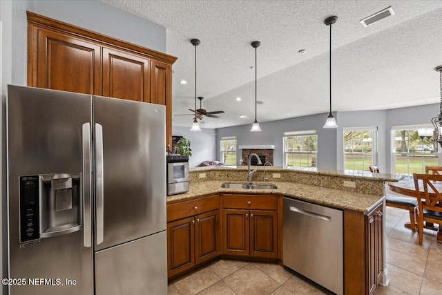 kitchen with a sink, visible vents, appliances with stainless steel finishes, brown cabinets, and pendant lighting