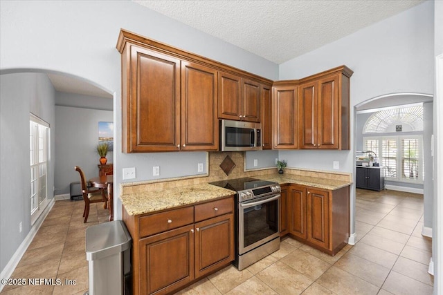 kitchen with stainless steel appliances, arched walkways, light tile patterned flooring, and light stone counters