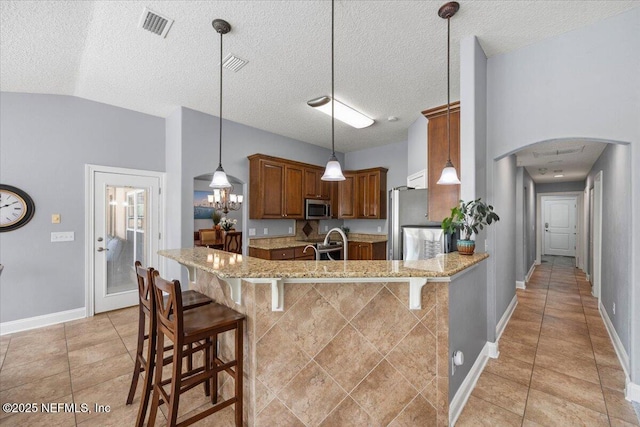 kitchen featuring visible vents, arched walkways, brown cabinets, stainless steel appliances, and a kitchen bar