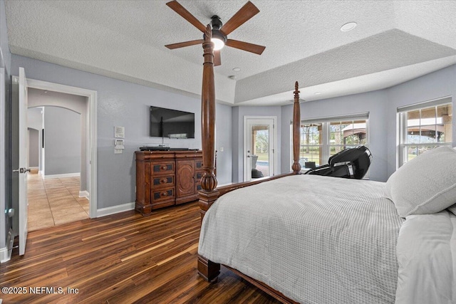 bedroom featuring arched walkways, a textured ceiling, wood finished floors, baseboards, and access to exterior