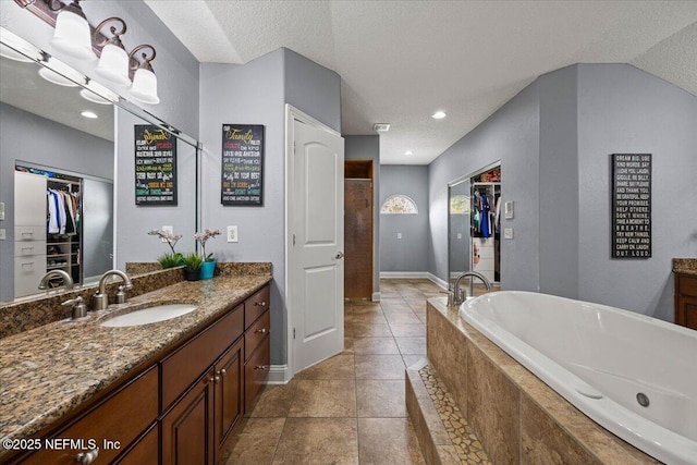 full bath featuring a relaxing tiled tub, a spacious closet, vanity, a textured ceiling, and tile patterned floors