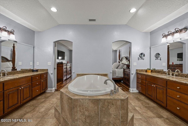 full bathroom featuring vaulted ceiling, two vanities, a sink, and a bath