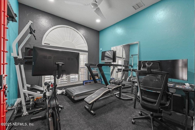 exercise room with visible vents, a textured wall, a textured ceiling, and ceiling fan