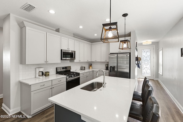 kitchen with stainless steel appliances, a sink, visible vents, light countertops, and tasteful backsplash