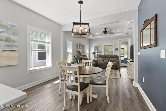 dining space with a notable chandelier, baseboards, a raised ceiling, and dark wood-type flooring