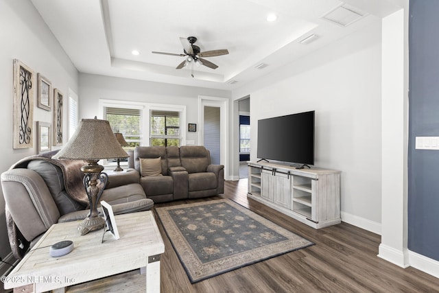 living room with a tray ceiling, recessed lighting, dark wood-type flooring, ceiling fan, and baseboards