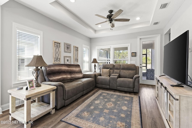 living area with baseboards, visible vents, wood finished floors, a tray ceiling, and recessed lighting