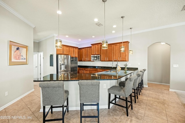 kitchen featuring arched walkways, brown cabinetry, a peninsula, stainless steel appliances, and a sink