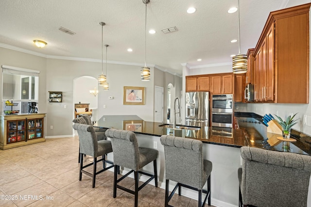 kitchen with arched walkways, brown cabinets, stainless steel appliances, visible vents, and a peninsula