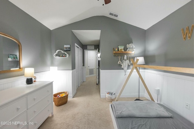 bedroom with light carpet, a wainscoted wall, visible vents, and vaulted ceiling