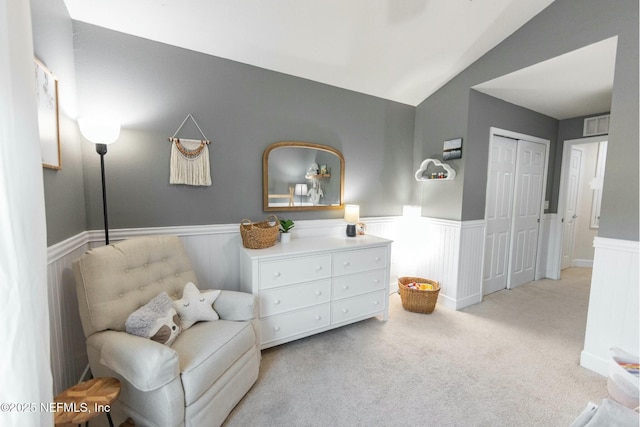 living area with lofted ceiling, visible vents, carpet flooring, and wainscoting