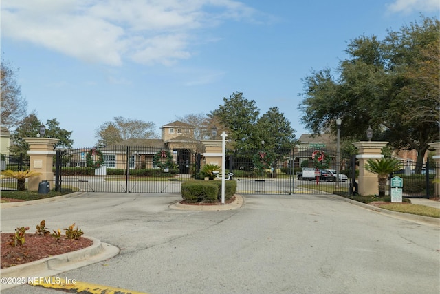 view of road featuring street lights, curbs, a gated entry, and a gate