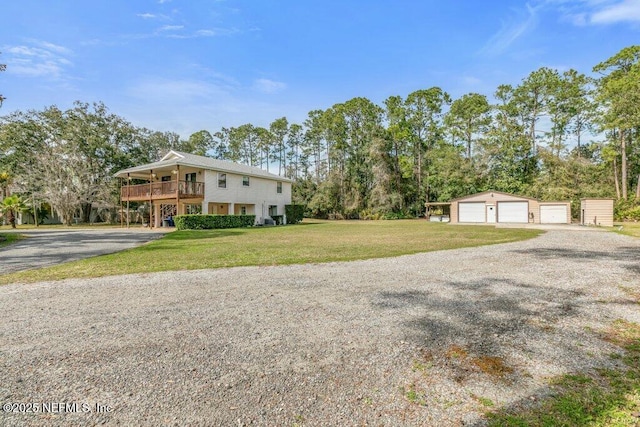 exterior space featuring an outbuilding, a detached garage, a wooden deck, a front lawn, and gravel driveway