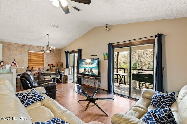 living area featuring a textured ceiling, ceiling fan with notable chandelier, wood finished floors, visible vents, and vaulted ceiling