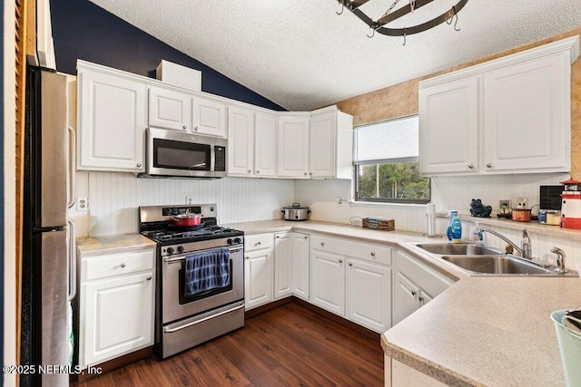 kitchen featuring dark wood finished floors, lofted ceiling, appliances with stainless steel finishes, white cabinetry, and a sink