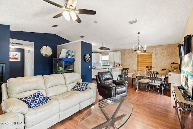 living area with lofted ceiling, ceiling fan, a textured ceiling, visible vents, and light wood finished floors