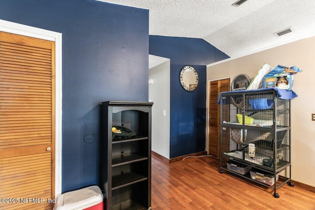 interior space with a textured ceiling, visible vents, vaulted ceiling, and wood finished floors