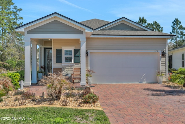 view of front facade with an attached garage, covered porch, decorative driveway, and roof with shingles