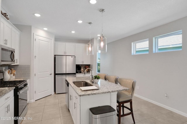 kitchen featuring tasteful backsplash, a center island with sink, appliances with stainless steel finishes, white cabinetry, and a sink