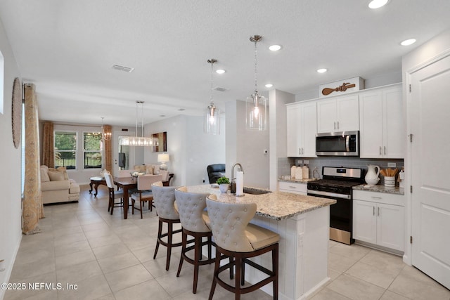 kitchen with stainless steel appliances, visible vents, decorative backsplash, white cabinets, and a sink