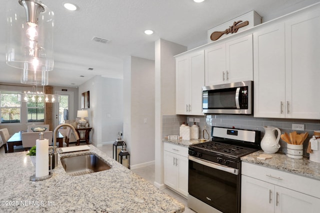 kitchen featuring stainless steel appliances, backsplash, white cabinetry, a sink, and light stone countertops