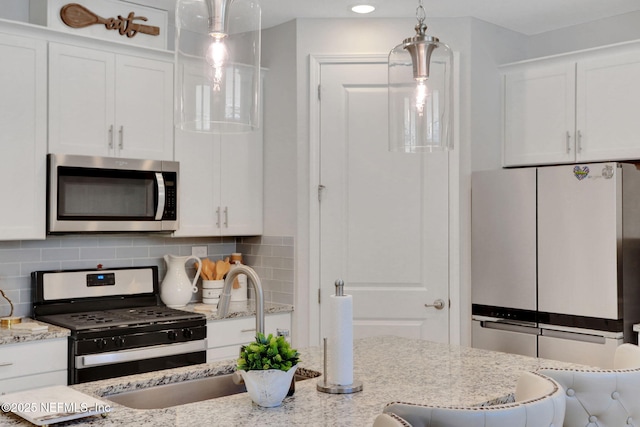 kitchen featuring white cabinets, appliances with stainless steel finishes, decorative backsplash, light stone countertops, and pendant lighting