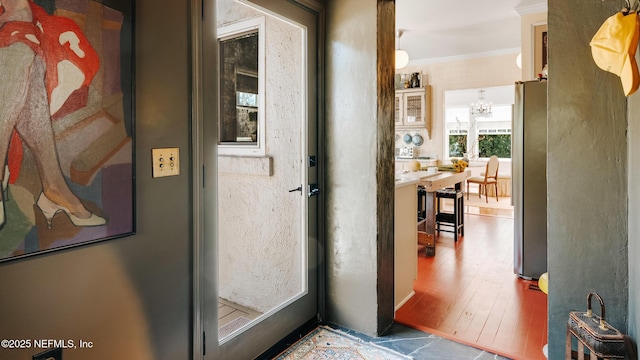 doorway to outside featuring a chandelier, crown molding, and wood finished floors